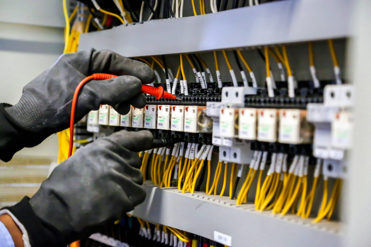 Electrician testing control panel wiring with multimeter and safety gloves