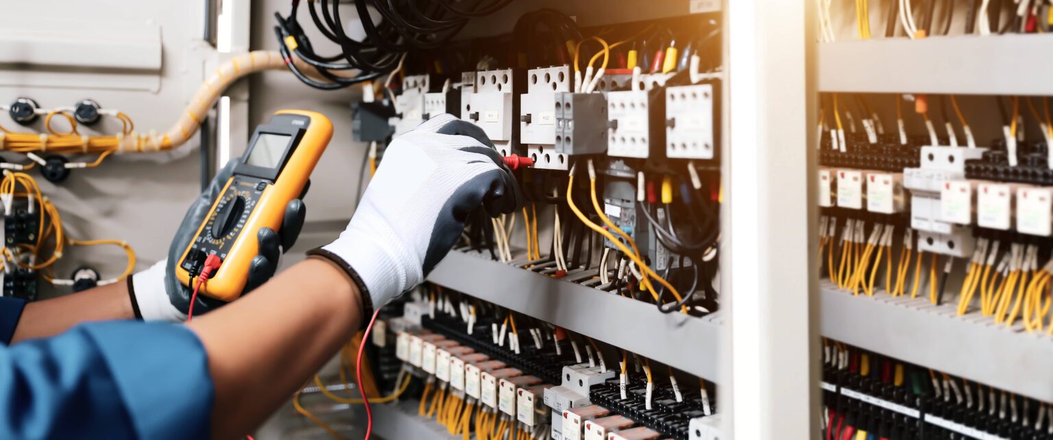 Electrician testing industrial control panel with multimeter for safety and maintenance
