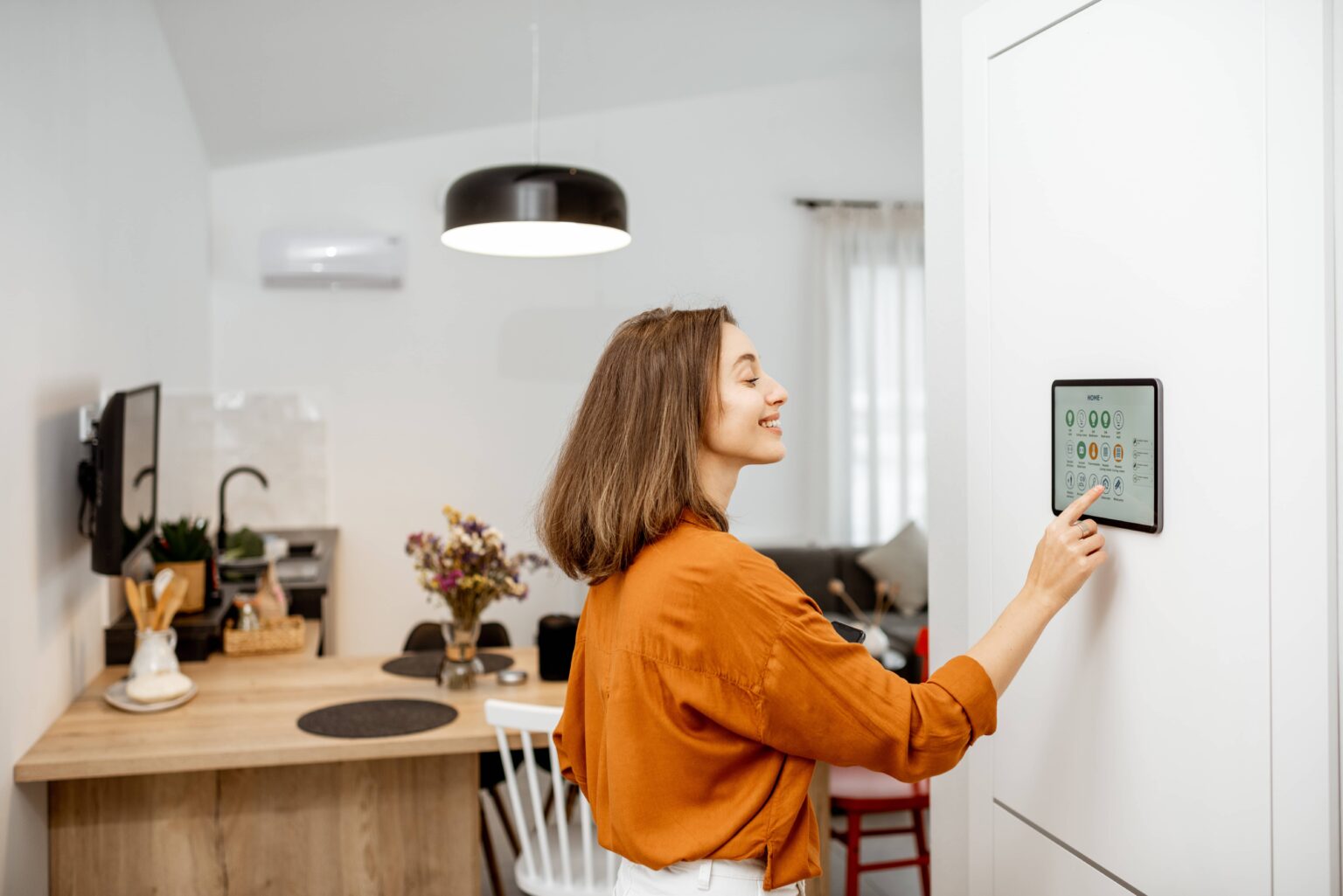 Woman using a smart home control panel in a modern kitchen and living space