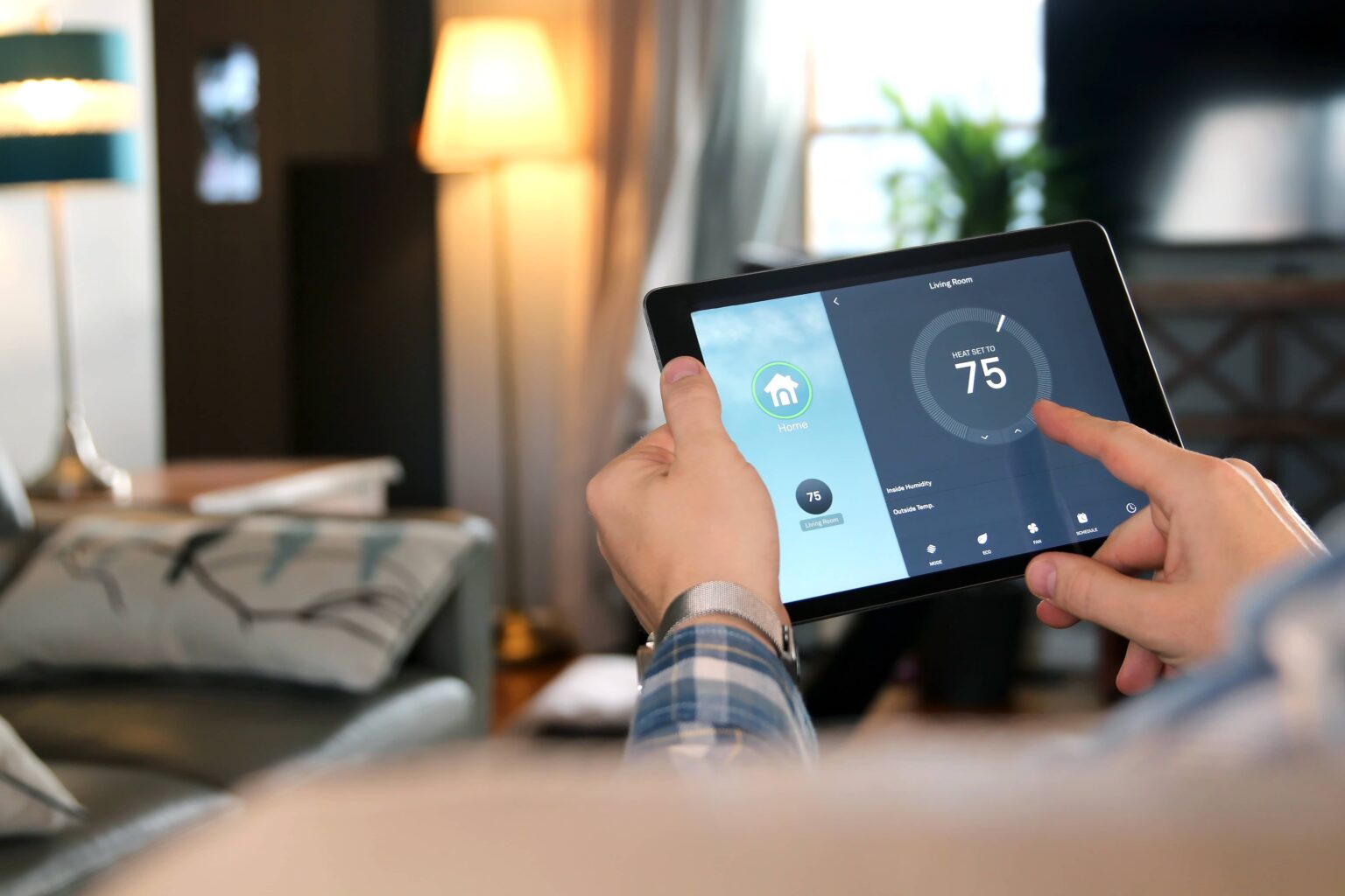 Person adjusting smart home thermostat settings on a tablet in a modern living room