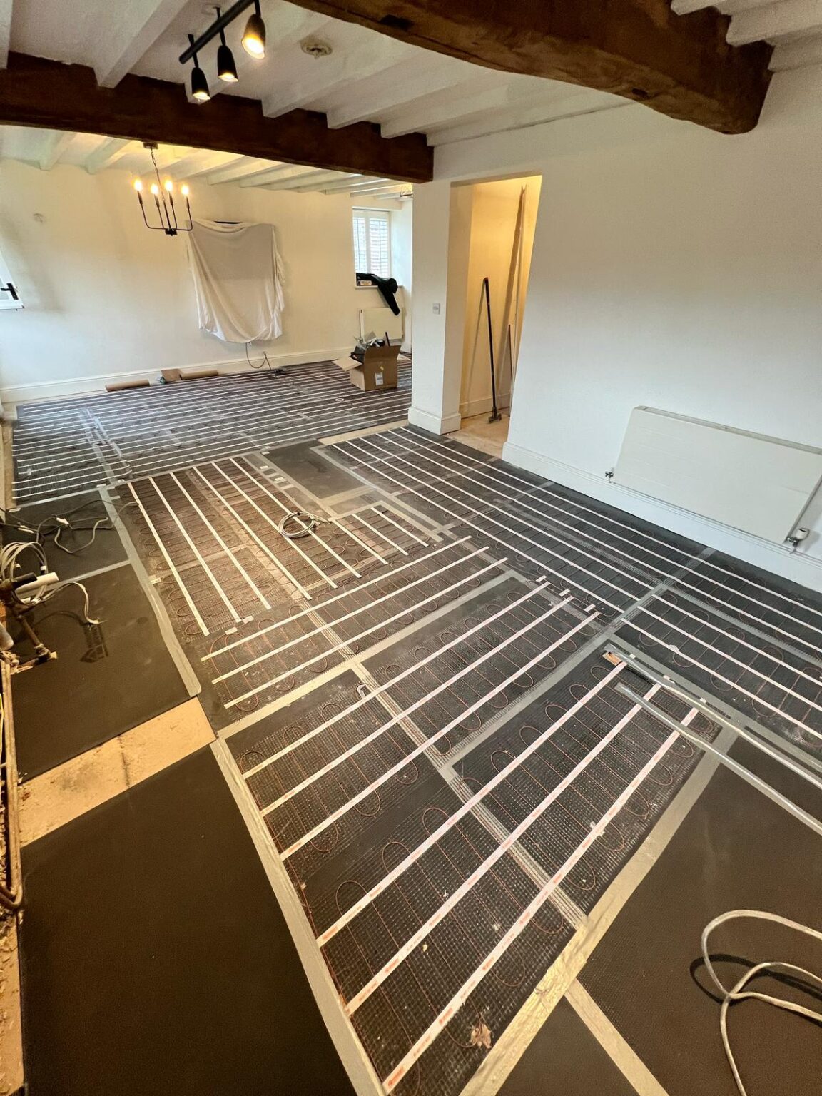 Underfloor heating installation in progress inside a renovated room with exposed beams and partially finished flooring