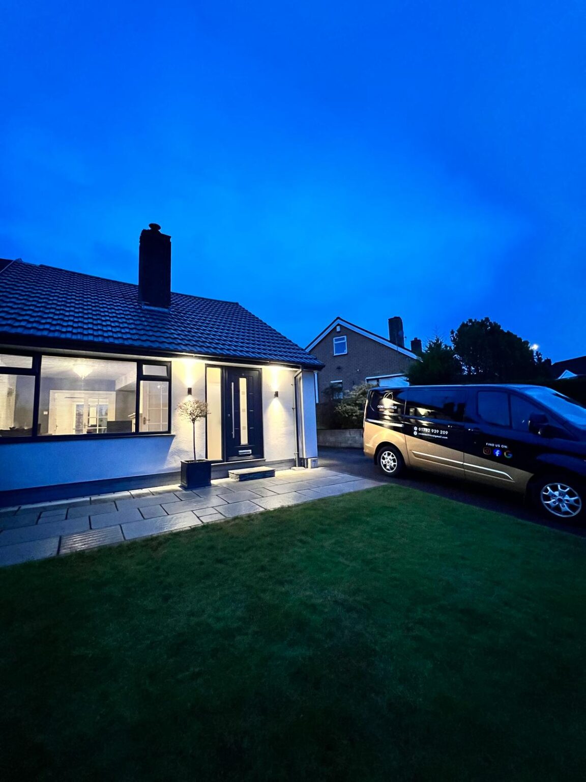 Modern bungalow exterior at dusk with lights on and a work van parked outside