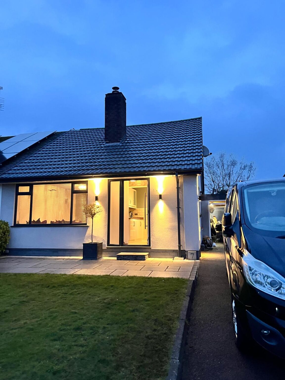 Modern bungalow with outdoor wall lighting and solar panels at dusk