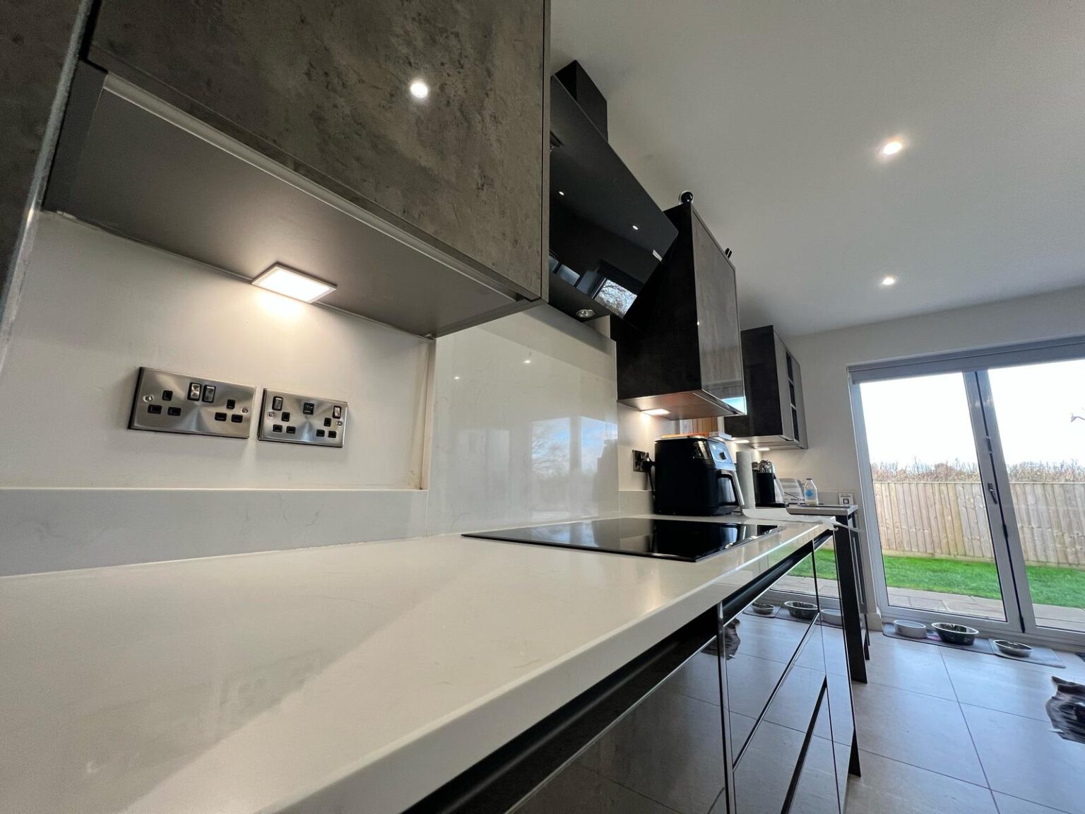 Modern kitchen worktop with under-cabinet lighting, stainless steel sockets, and induction hob