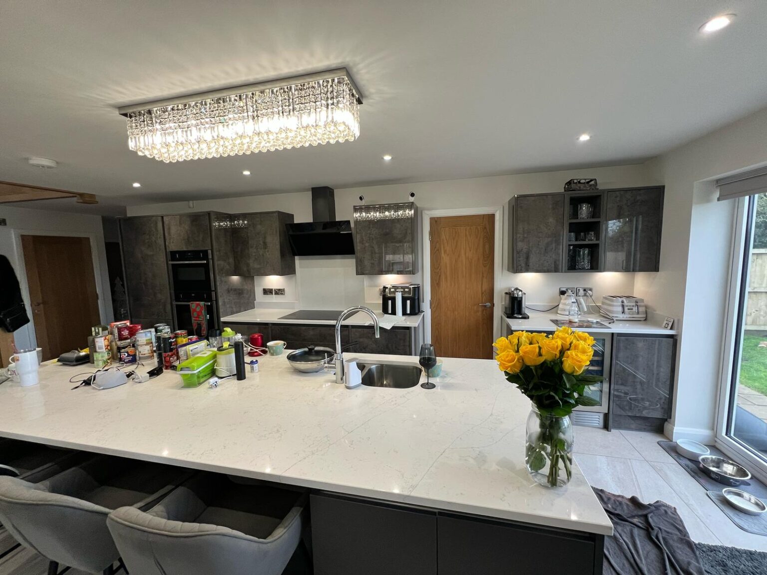 Modern grey kitchen with marble island countertop, crystal ceiling light, and a vase of yellow roses
