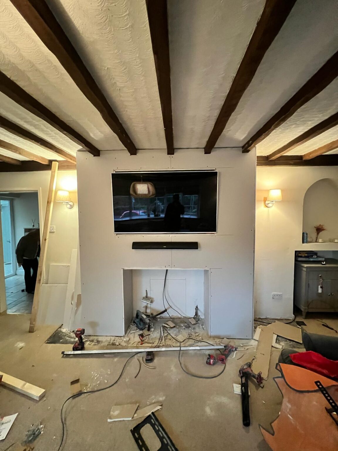Living room renovation in progress with TV wall installation, exposed wiring, and tools on the floor