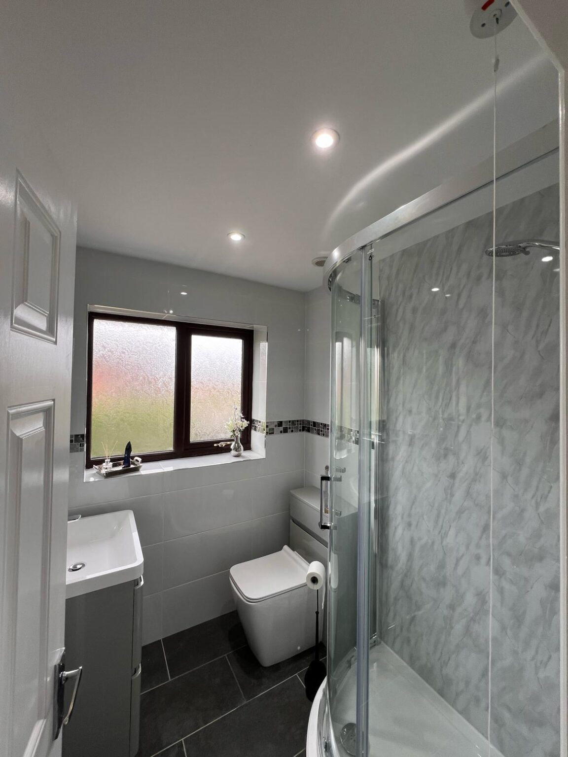 Modern bathroom with walk-in shower, LED lighting, and sleek grey tile finish