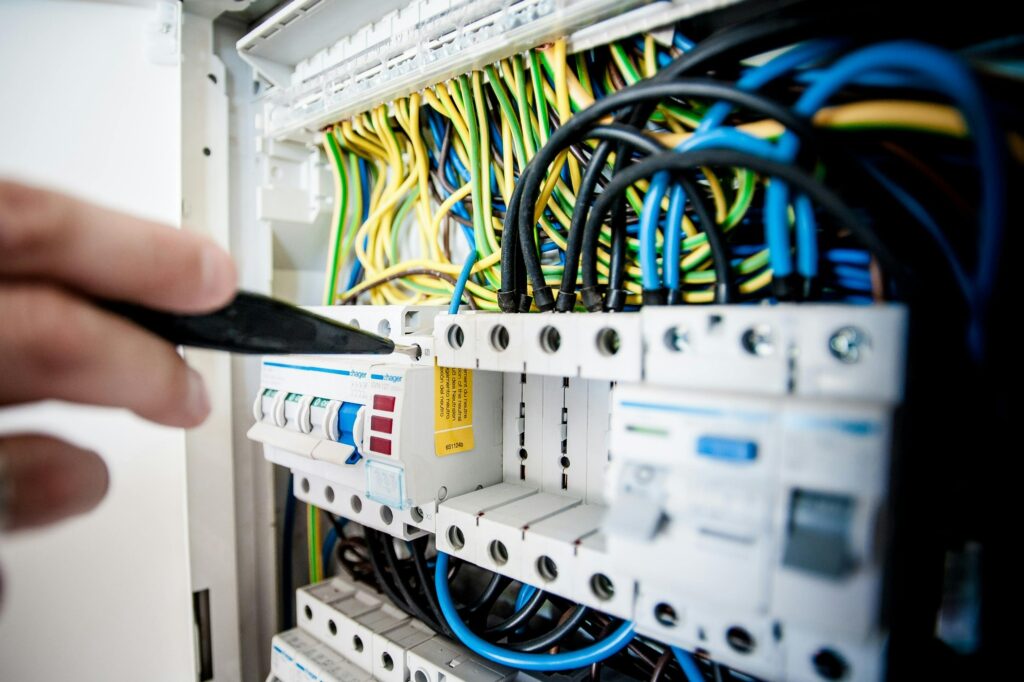 Electrician inspecting consumer unit with circuit breakers and wiring inside electrical distribution board